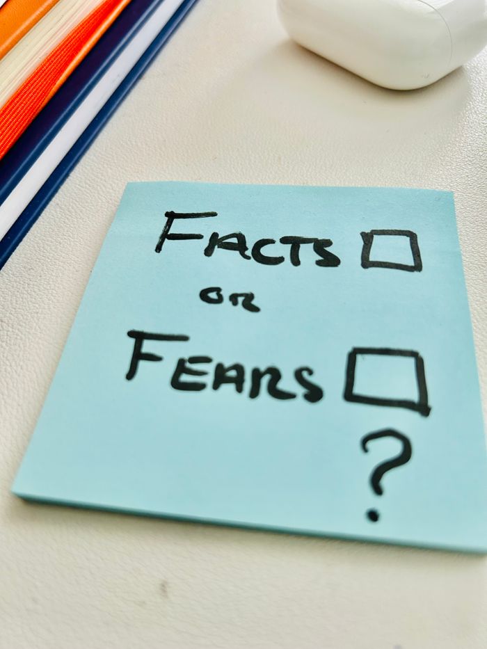 A blue sticky note asking "Facts or Fears" placed on a desk, prompting reflection.