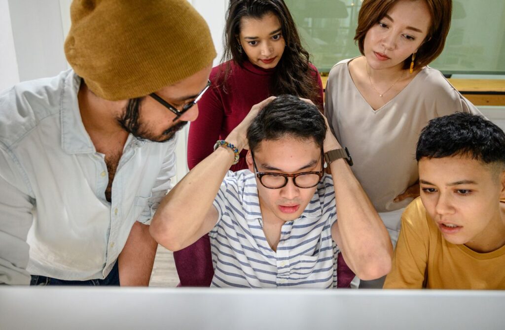 Five young adults working together on a project, looking concerned and focused at a computer screen.
